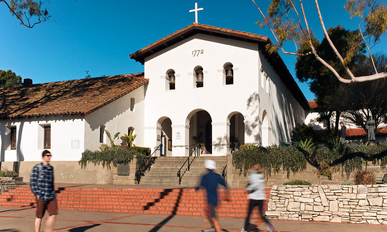 Entrance to San Luis Obispo Mission de Tolosa with pedestrian and joggers on sidewalk in foreground