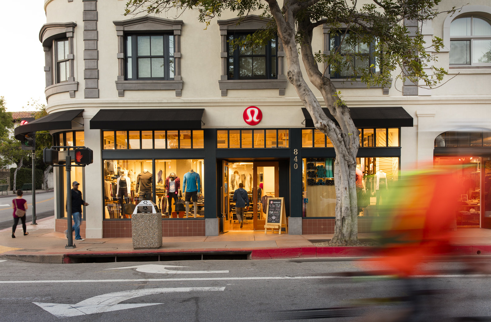 lululemon athletica storefront with pedestrians on sidewalk and bicyclist zooming by in street